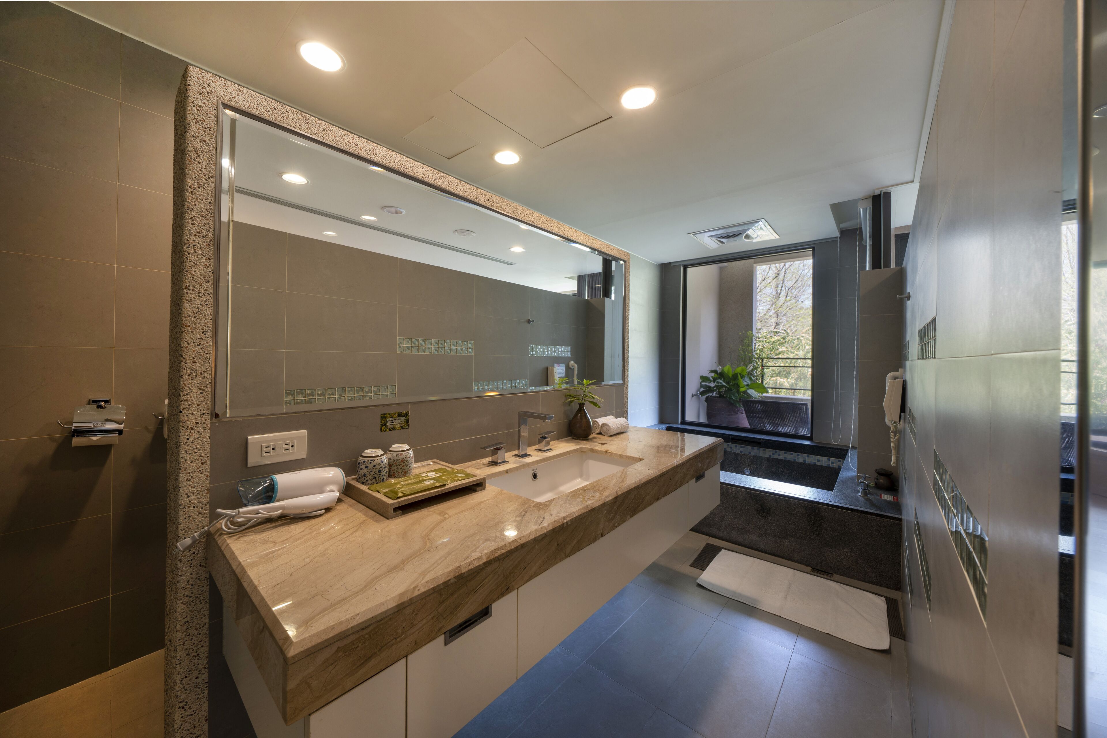 Un baño moderno con un lavamanos grande, espejo y ventana con vistas al exterior.