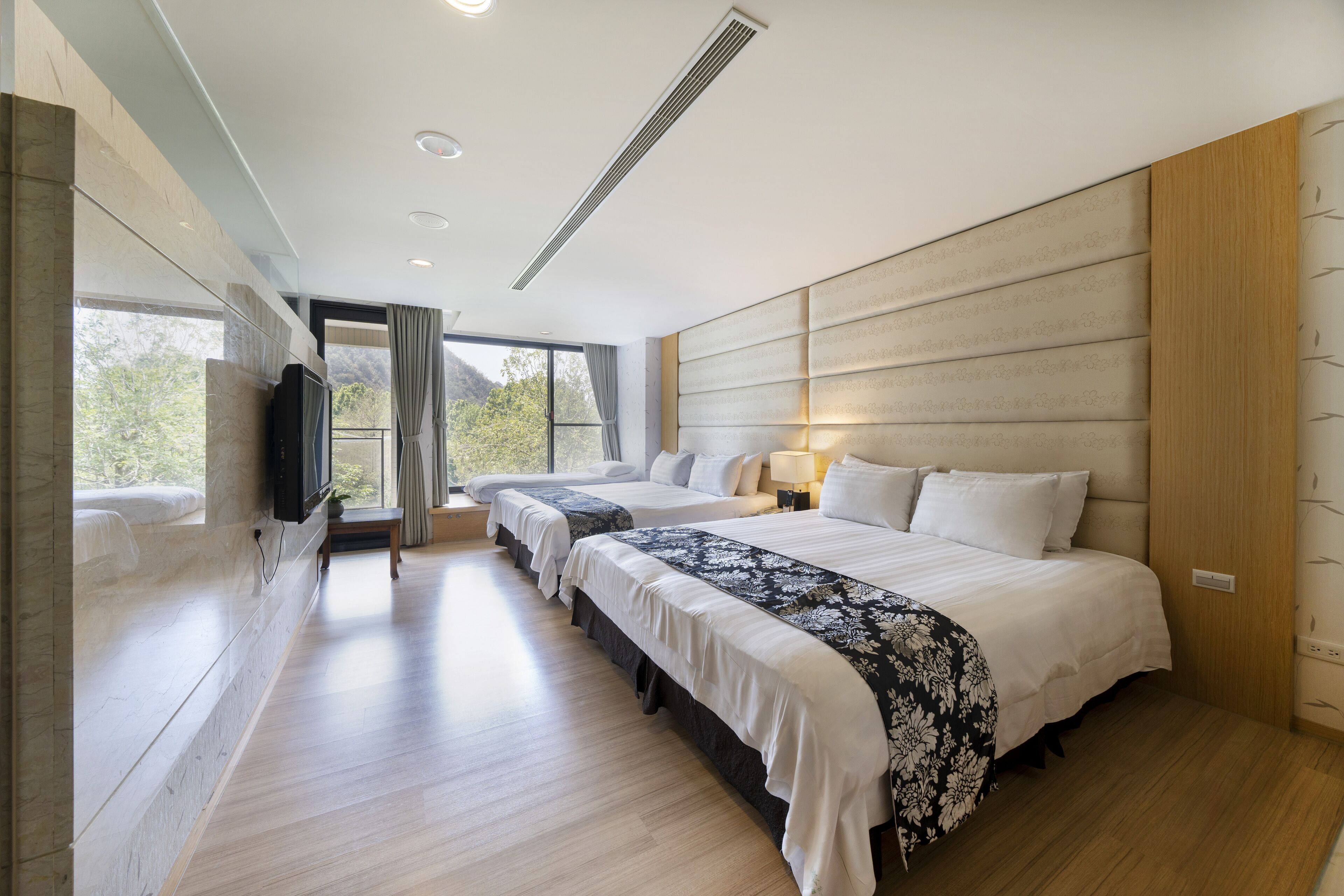 A modern hotel room with a large bed, two smaller beds, a TV, and a view of the outdoors.