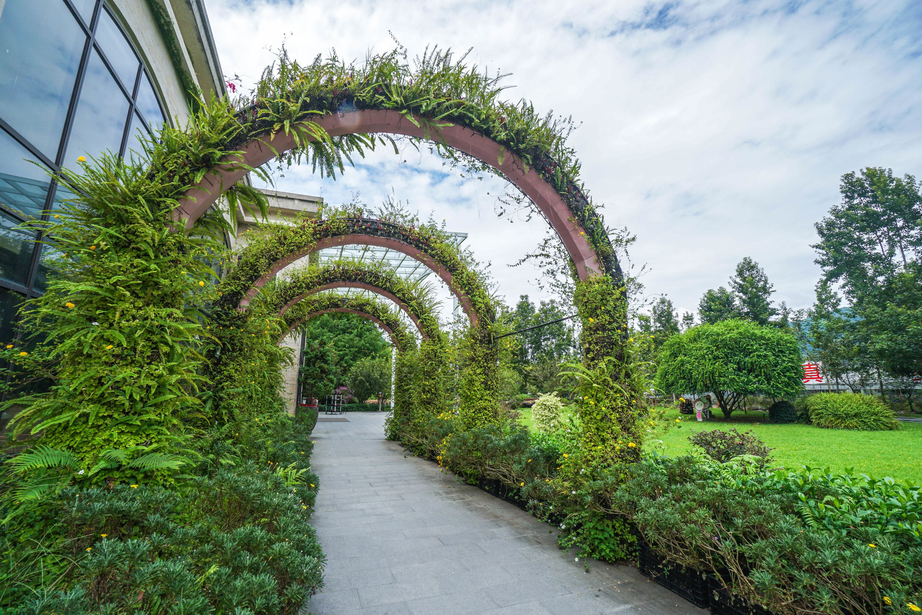 A pathway lined with lush greenery and an archway leading to a building.