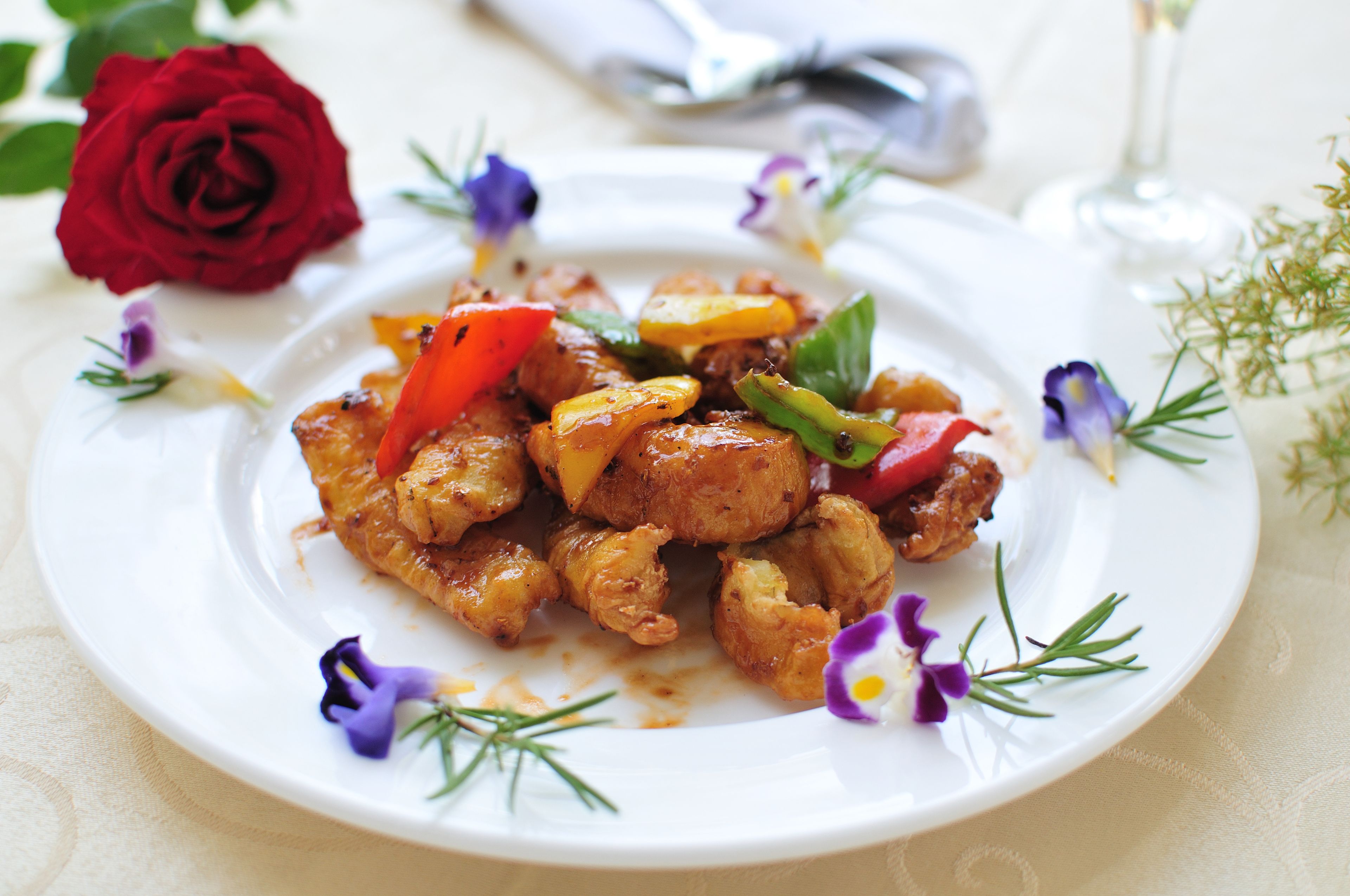 A plate of food with vegetables and herbs, surrounded by flowers and a rose.