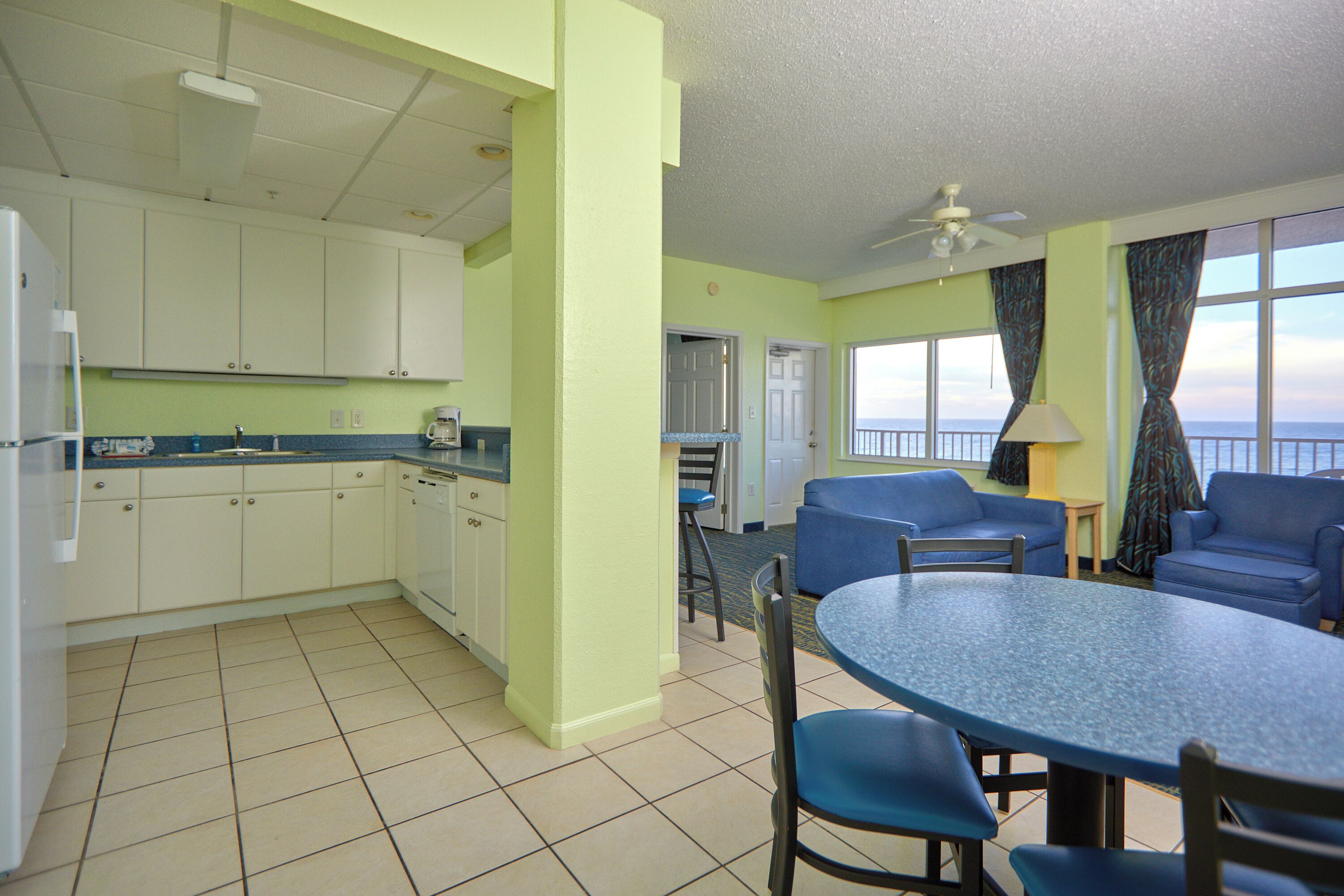 A kitchen with white cabinets, a dining table with chairs, and a view of the ocean through large windows.