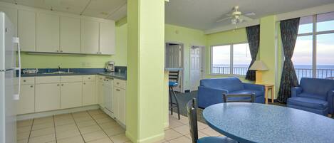A kitchen with white cabinets, a dining table with chairs, and a view of the ocean through large windows.