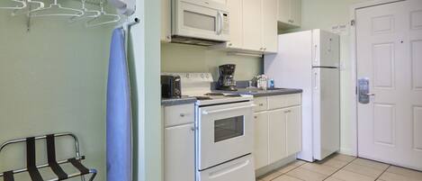 A compact kitchen with white cabinets, a microwave, a stove, and a refrigerator. There is a small sink and a towel rack.