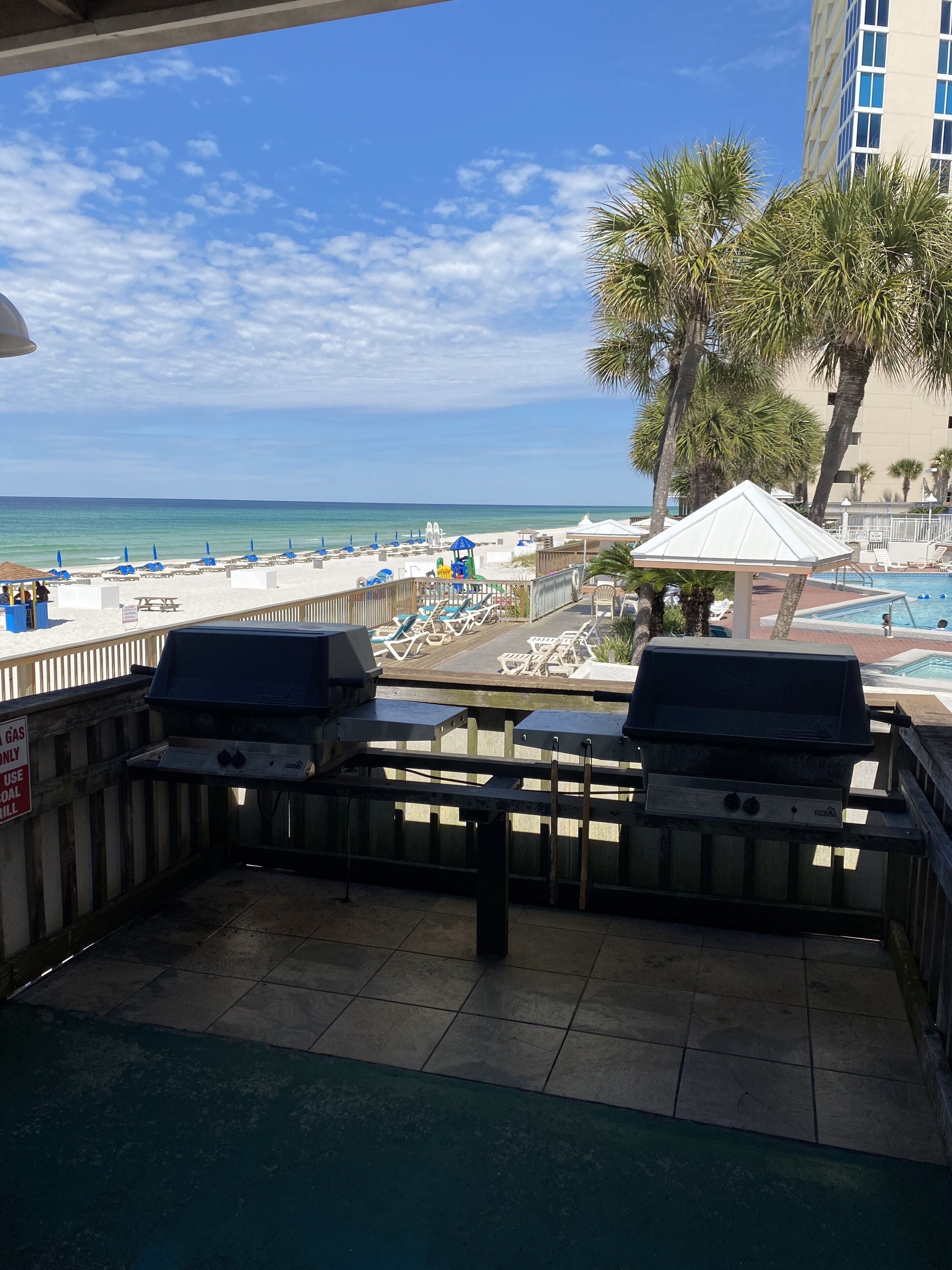A poolside area with lounge chairs, a barbecue grill, and a view of the beach and ocean.