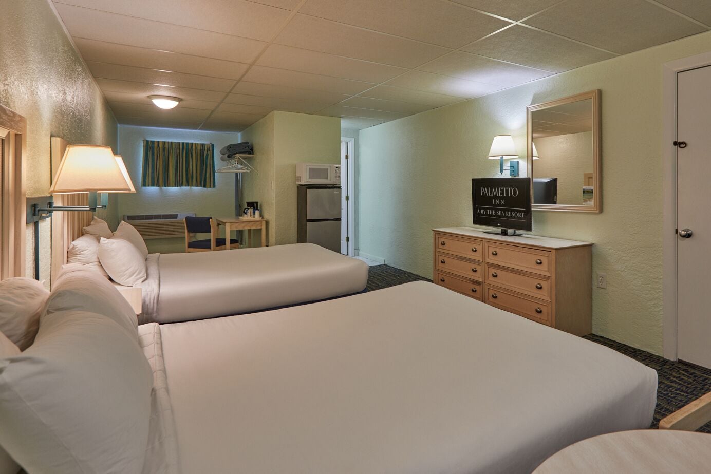 A hotel room with two beds, a desk, a dresser, and a television.