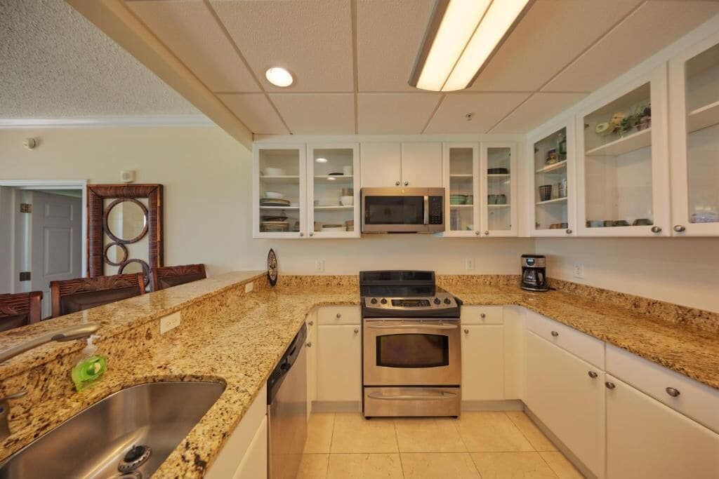 A kitchen with granite countertops, stainless steel appliances, white cabinetry, and a microwave above the stove.