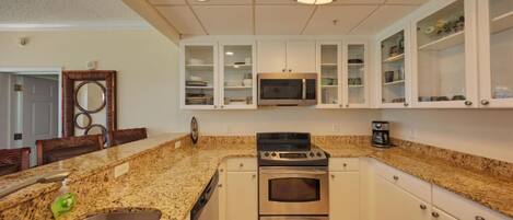 A kitchen with granite countertops, stainless steel appliances, white cabinetry, and a microwave above the stove.