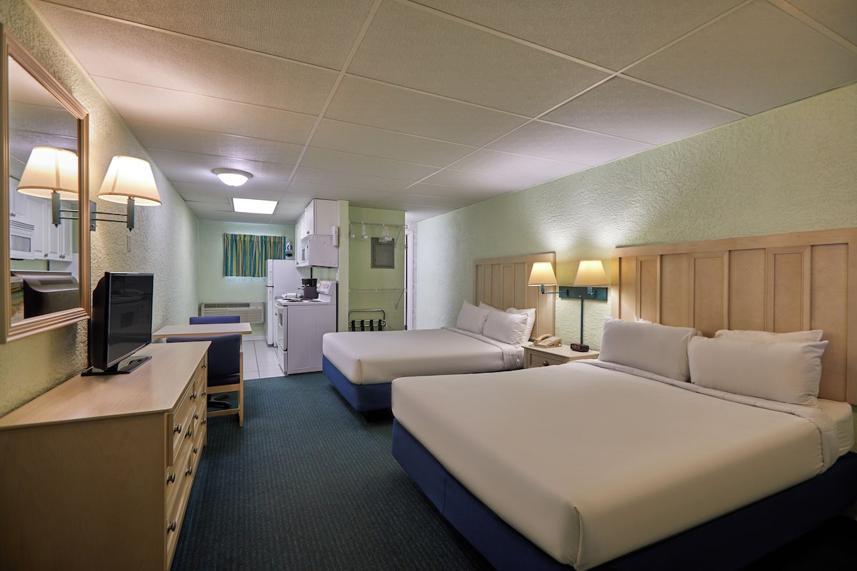 A hotel room with two beds, a desk, a television, and a kitchenette.