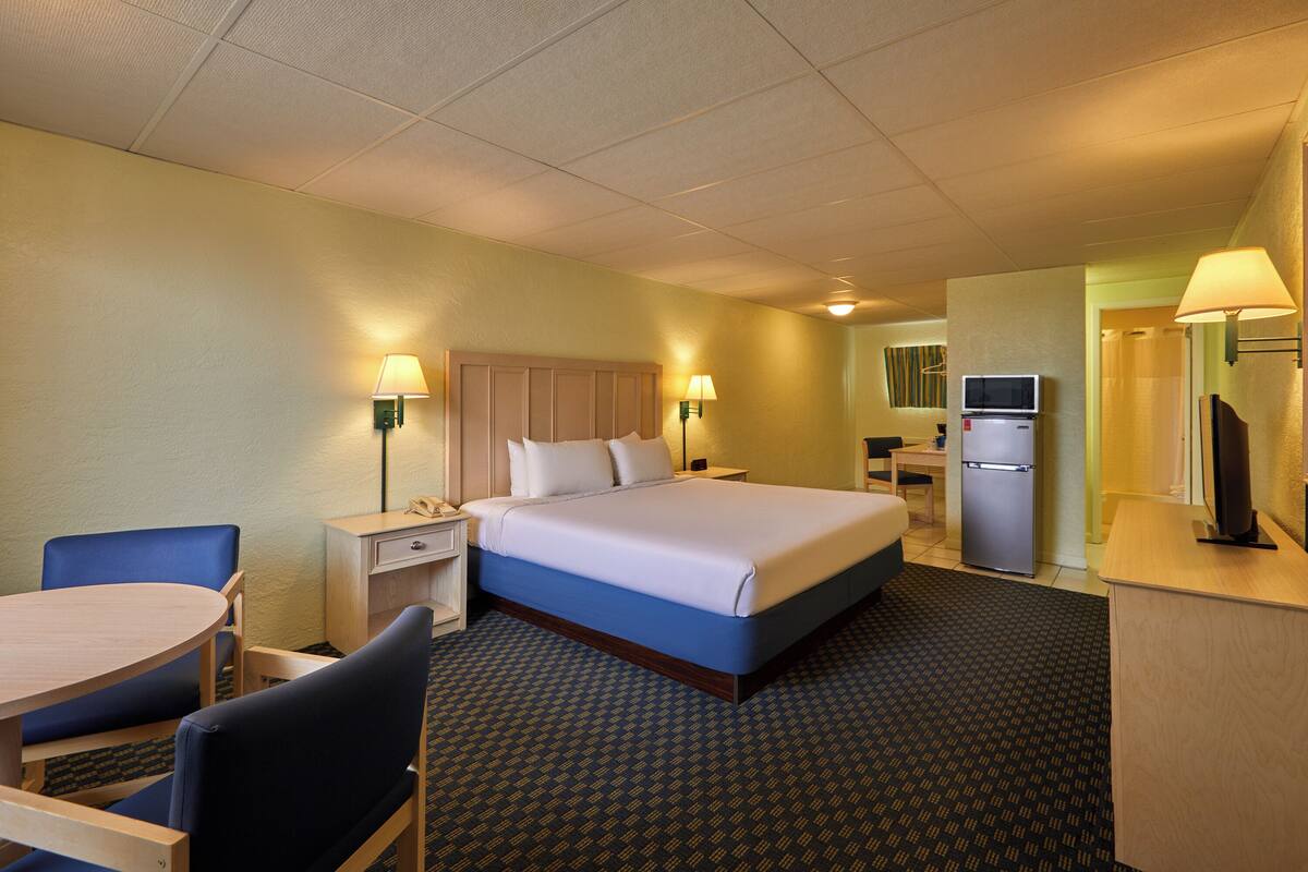A hotel room with a bed, desk, chair, lamp, and a television.