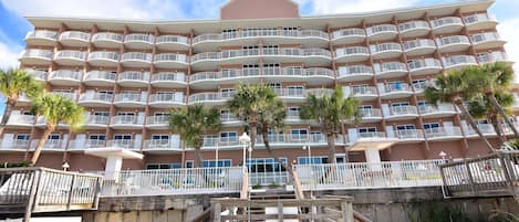 A multi-story hotel with balconies, a beachside location, and palm trees.
