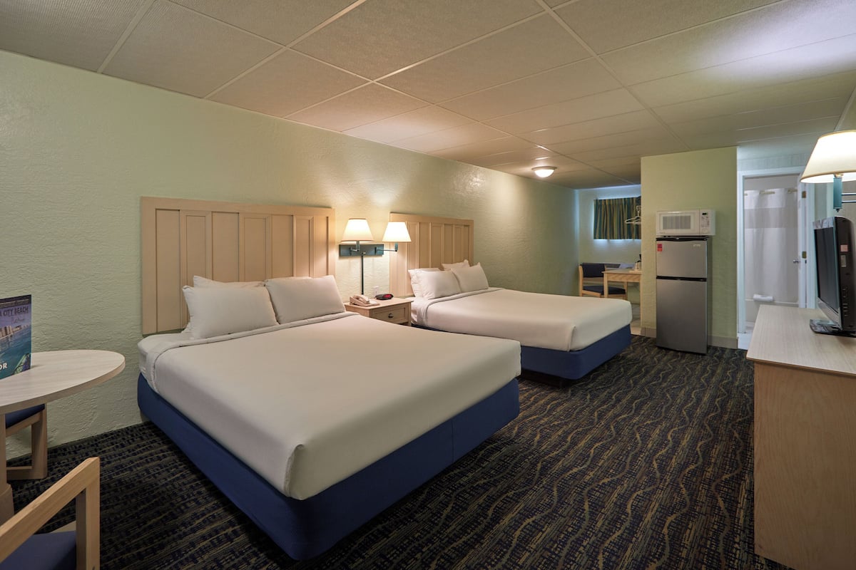 A hotel room with two beds, a desk, a chair, a microwave, a refrigerator, and a television.