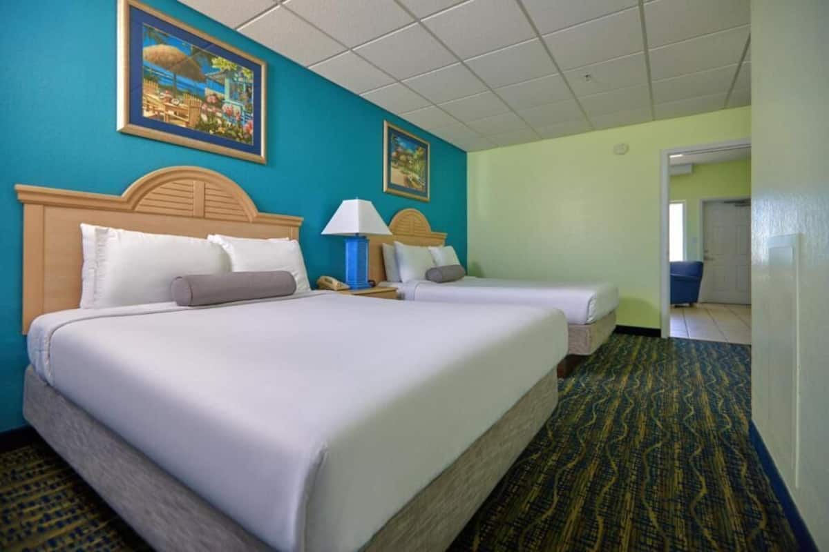 A hotel room with two beds, a nightstand with a lamp, and a view of the hallway.