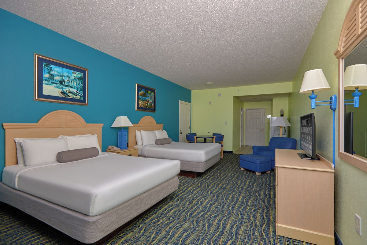 A hotel room with two beds, a desk, a chair, a TV, and a door leading to another room.