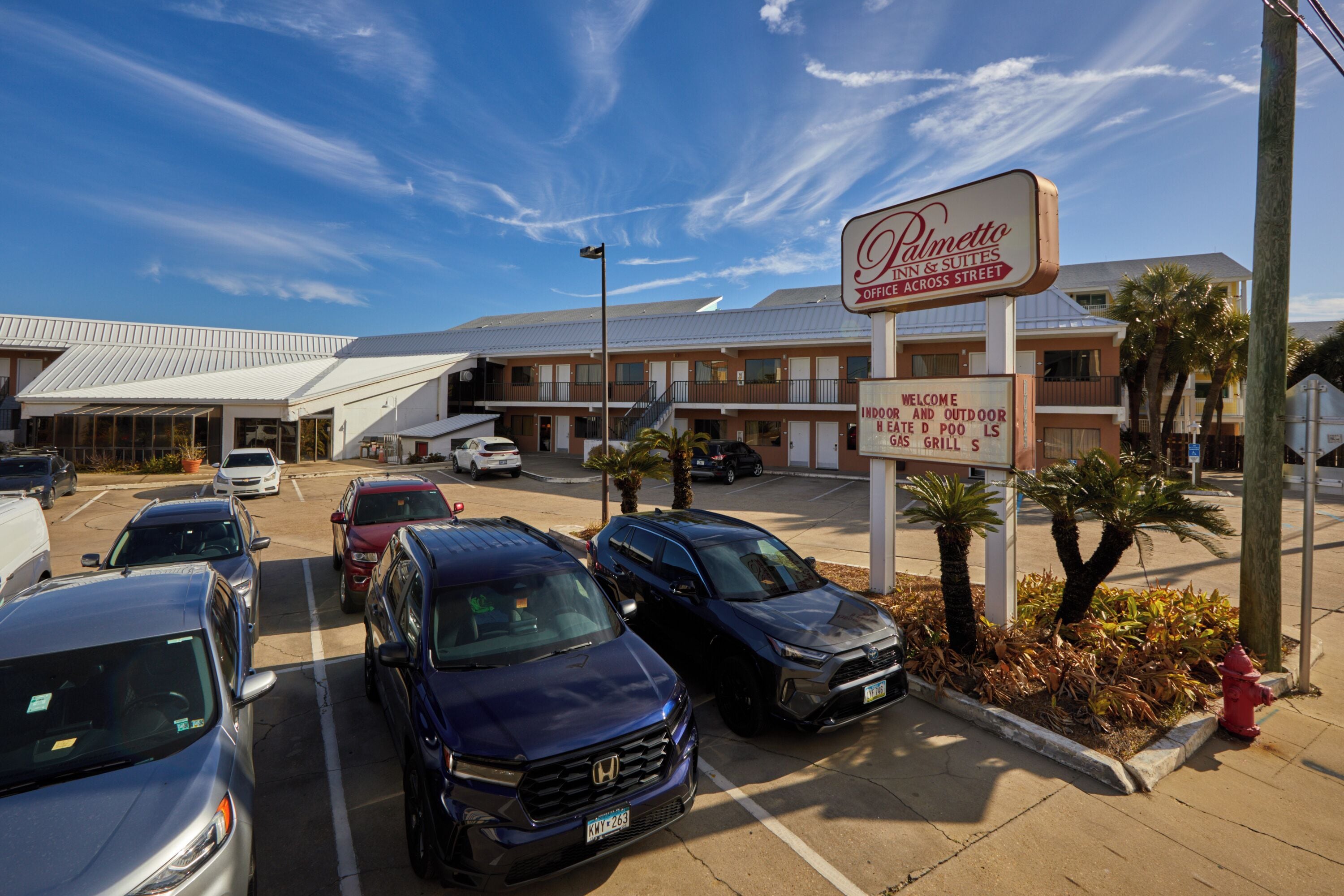 A parking lot with several cars, a hotel sign, and a building with a sloped roof.