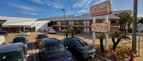 Un estacionamiento con varios autos, un letrero de hotel y un edificio de techo inclinado.