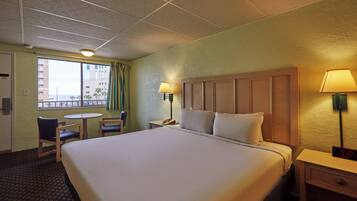 Habitación de hotel con una cama grande, un escritorio con lámpara, una silla, una mesita y un ventanal con cortinas.