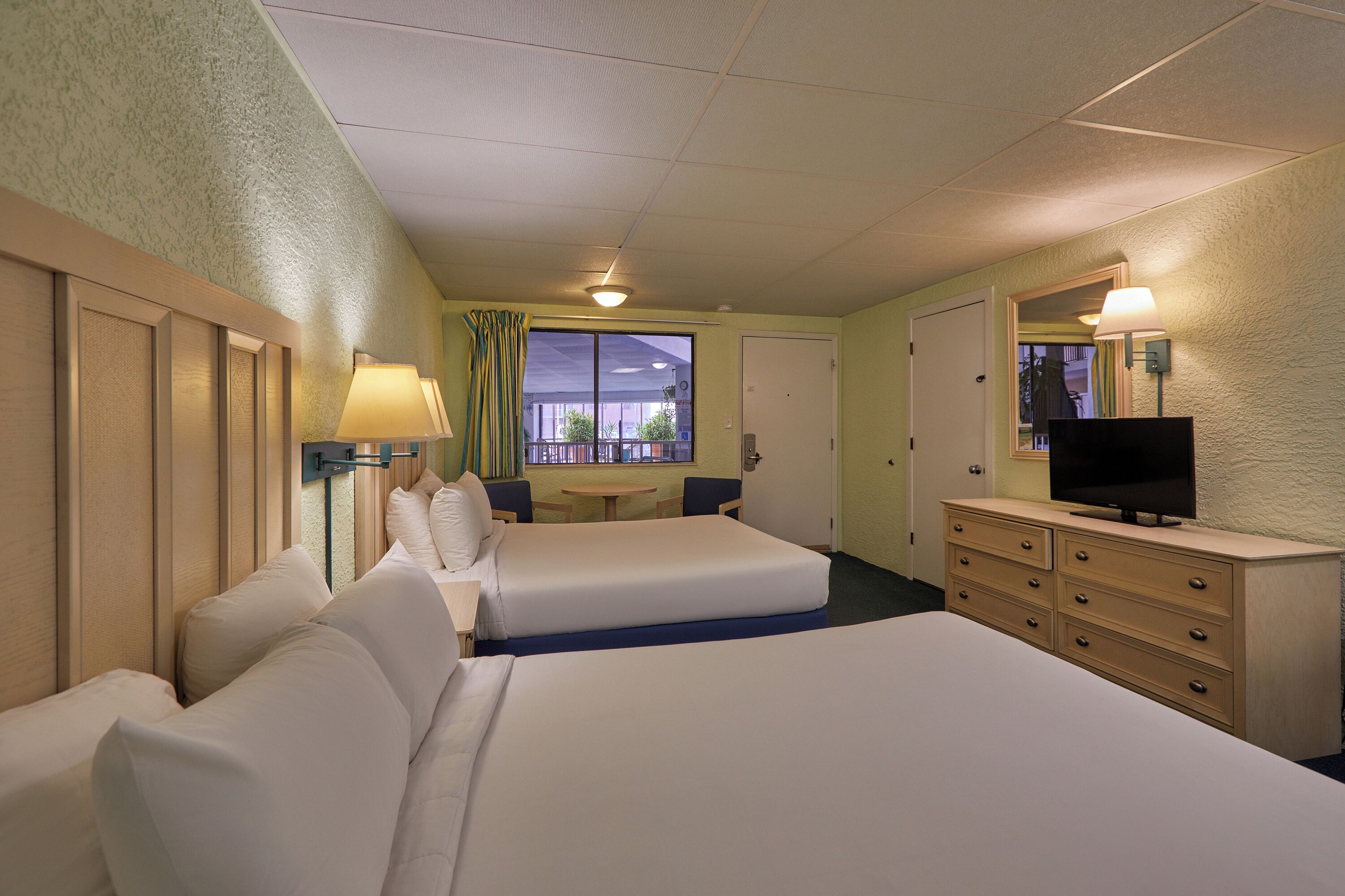 A hotel room with two beds, a desk, a chair, a dresser, a TV, and a window with a view.