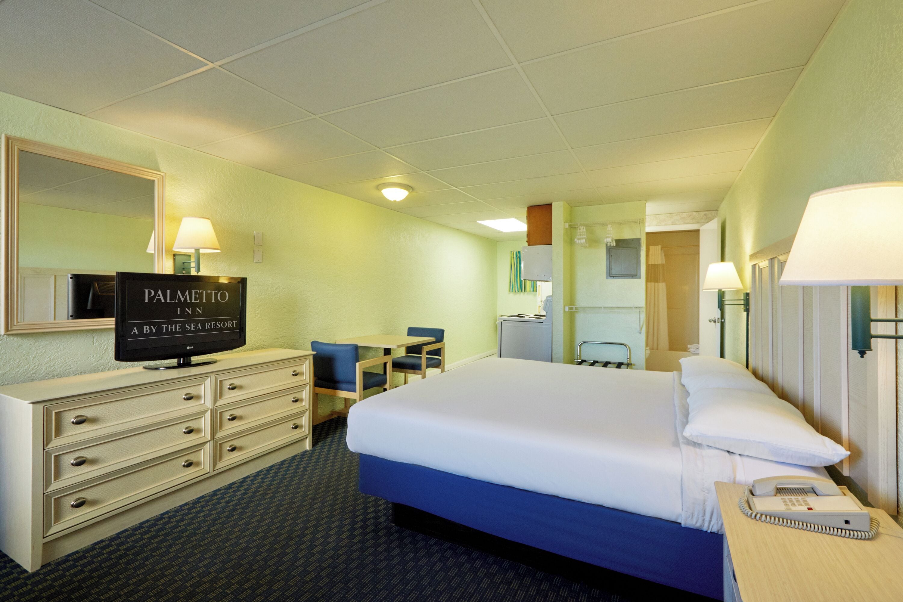 A hotel room with a bed, a desk, a chair, a TV, and a telephone.