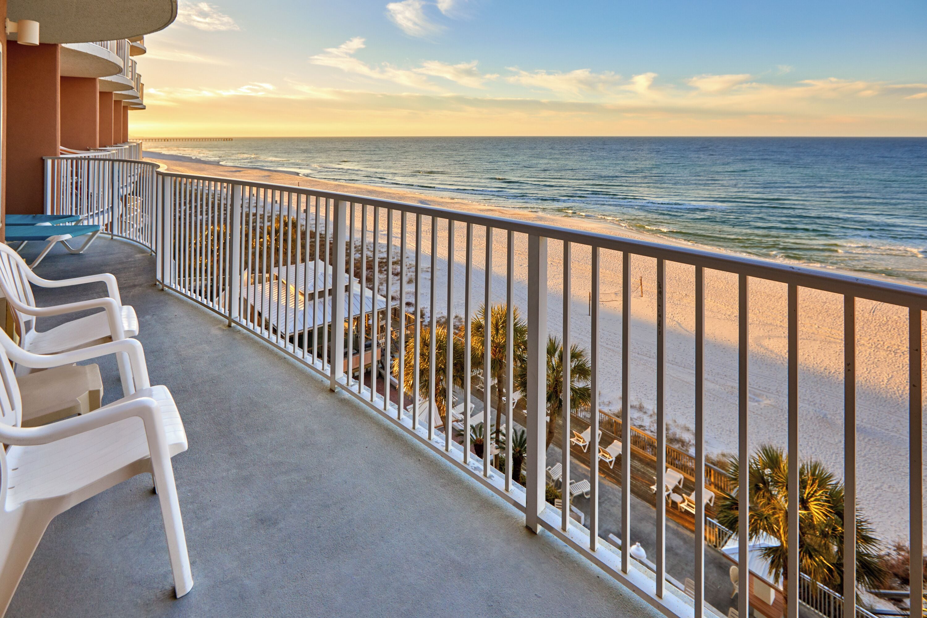 Un balcon avec des chaises blanches, une balustrade et une vue sur la plage et l’océan.