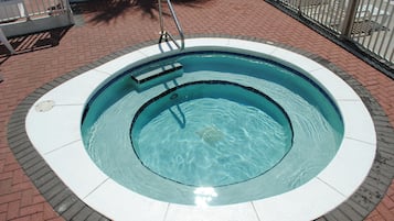 A circular hot tub with a tiled edge, surrounded by a brick patio and a metal fence.