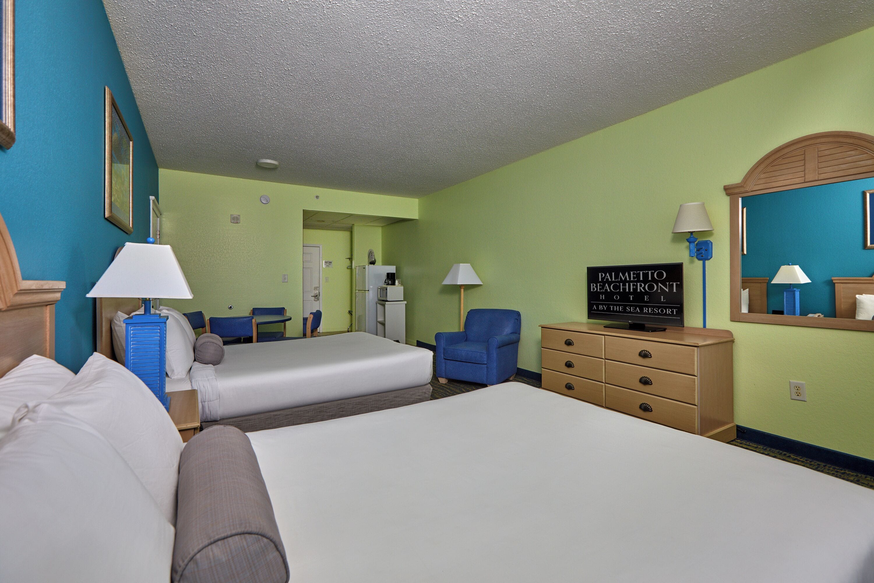 Une chambre d’hôtel avec deux lits, une commode, une chaise, un bureau et une enseigne indiquant le nom de l’hôtel.