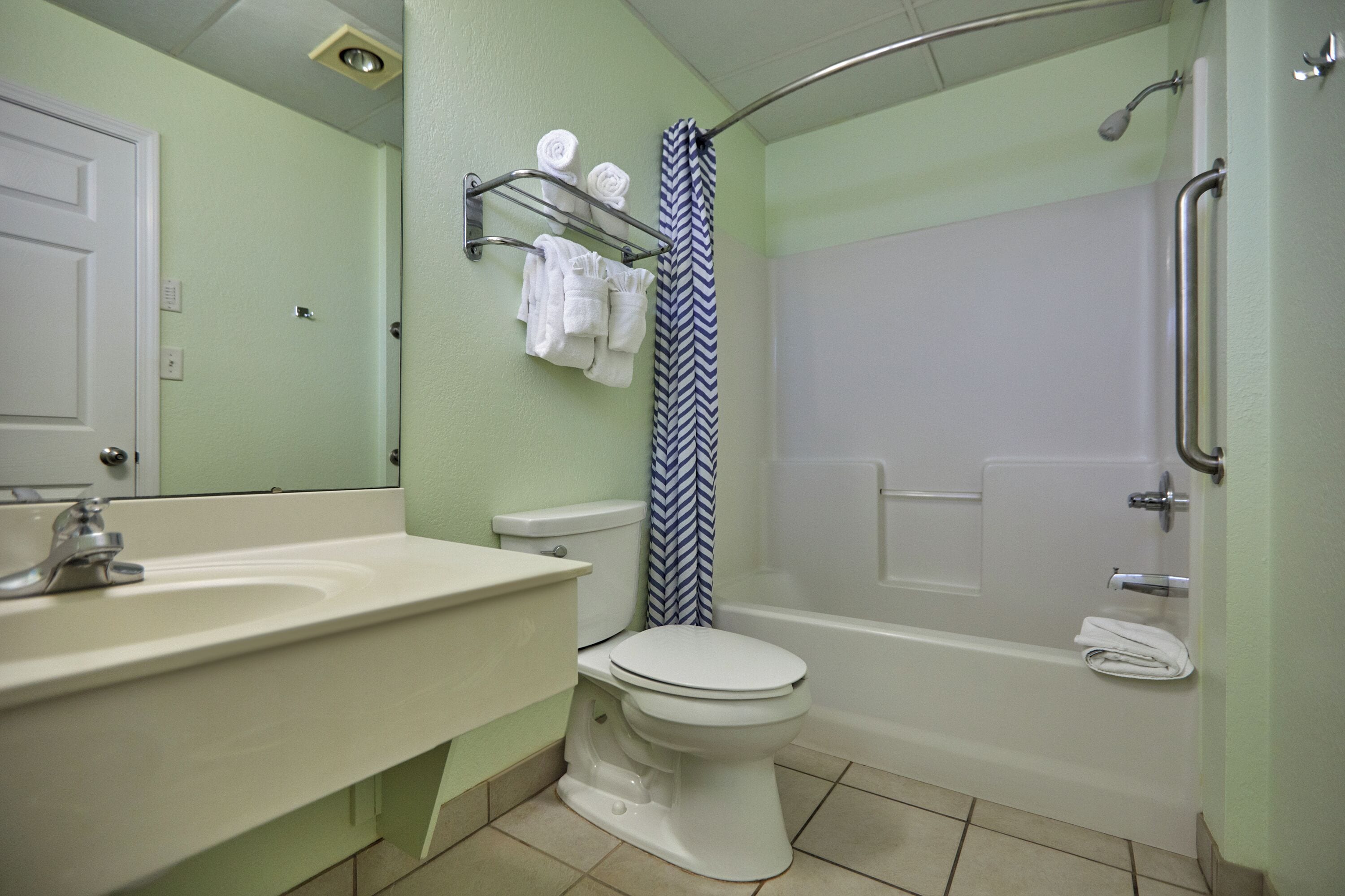 A bathroom with a toilet, sink, shower, and a towel rack.