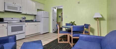 A compact kitchen with white appliances, a dining area with blue chairs, and a green wall.