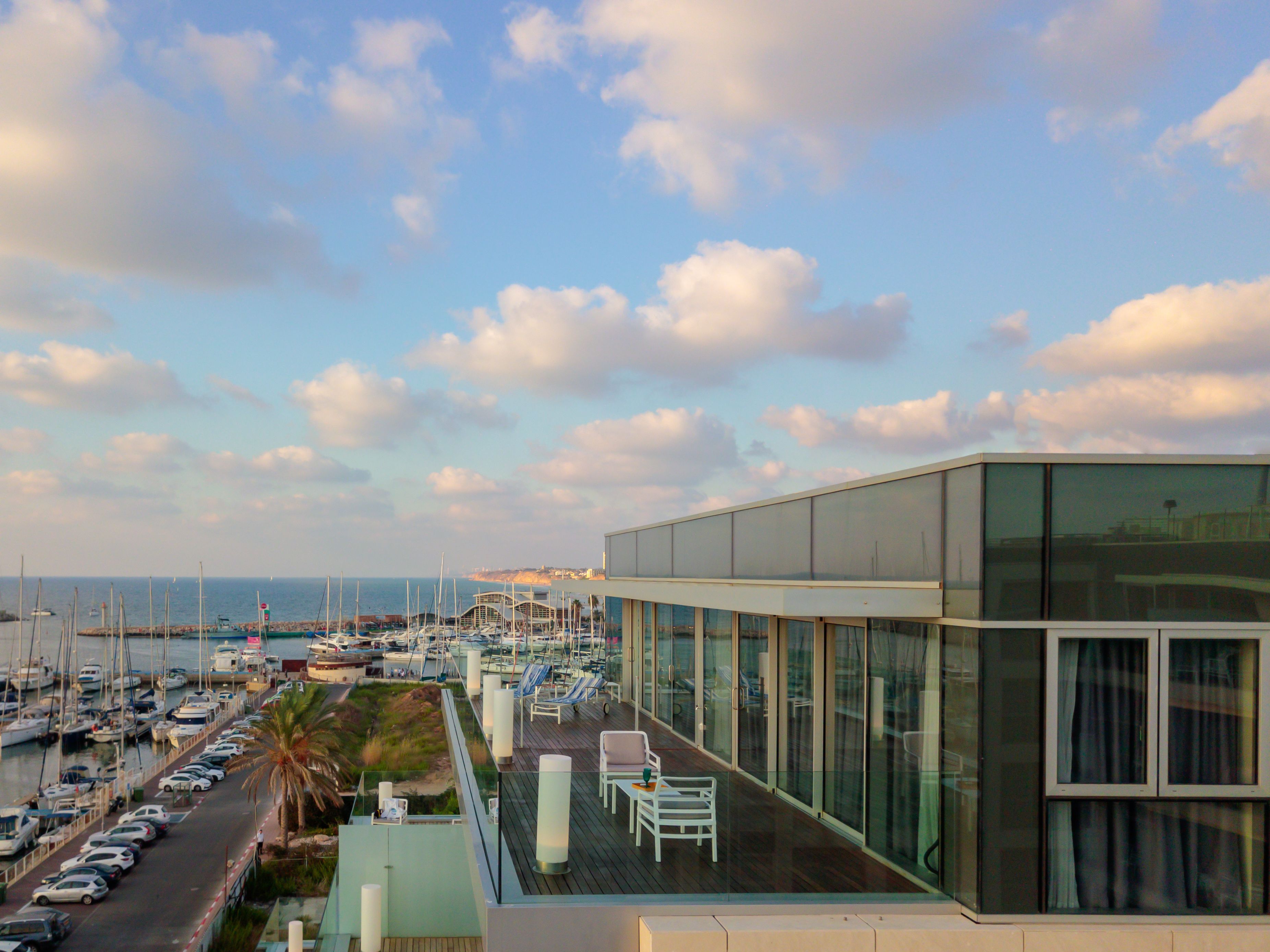 A modern building with a rooftop terrace overlooking a marina with boats and a coastal view.