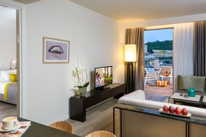 Une chambre d’hôtel comprenant un lit, une télévision, un coin repas avec une table et des chaises, un balcon offrant une vue sur le paysage, et une plante décorative.