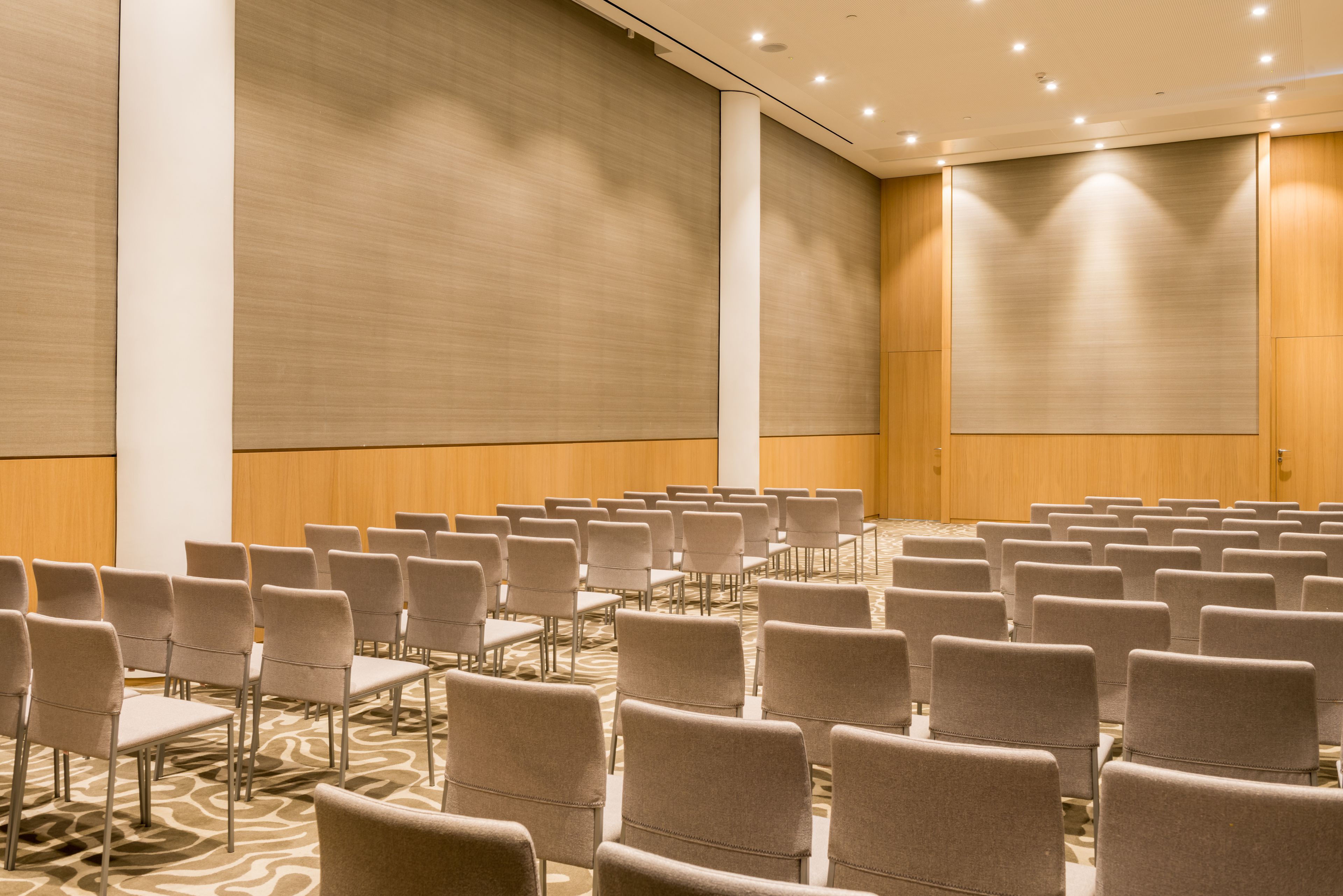 Un salón de conferencias con filas de sillas, una alfombra estampada y paneles de madera.