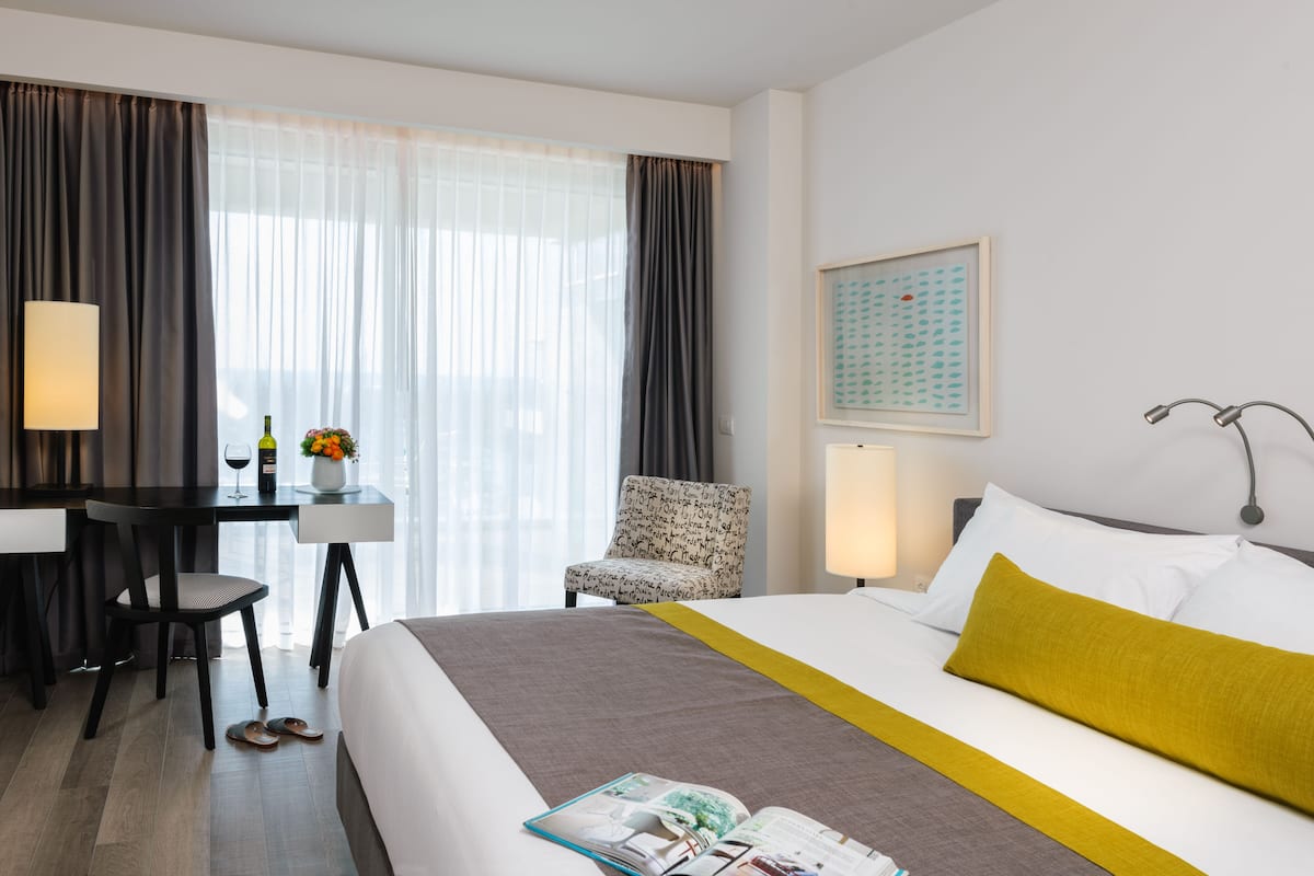 Een hotelkamer met een bed, bureau, stoel, lamp en raam met gordijnen.