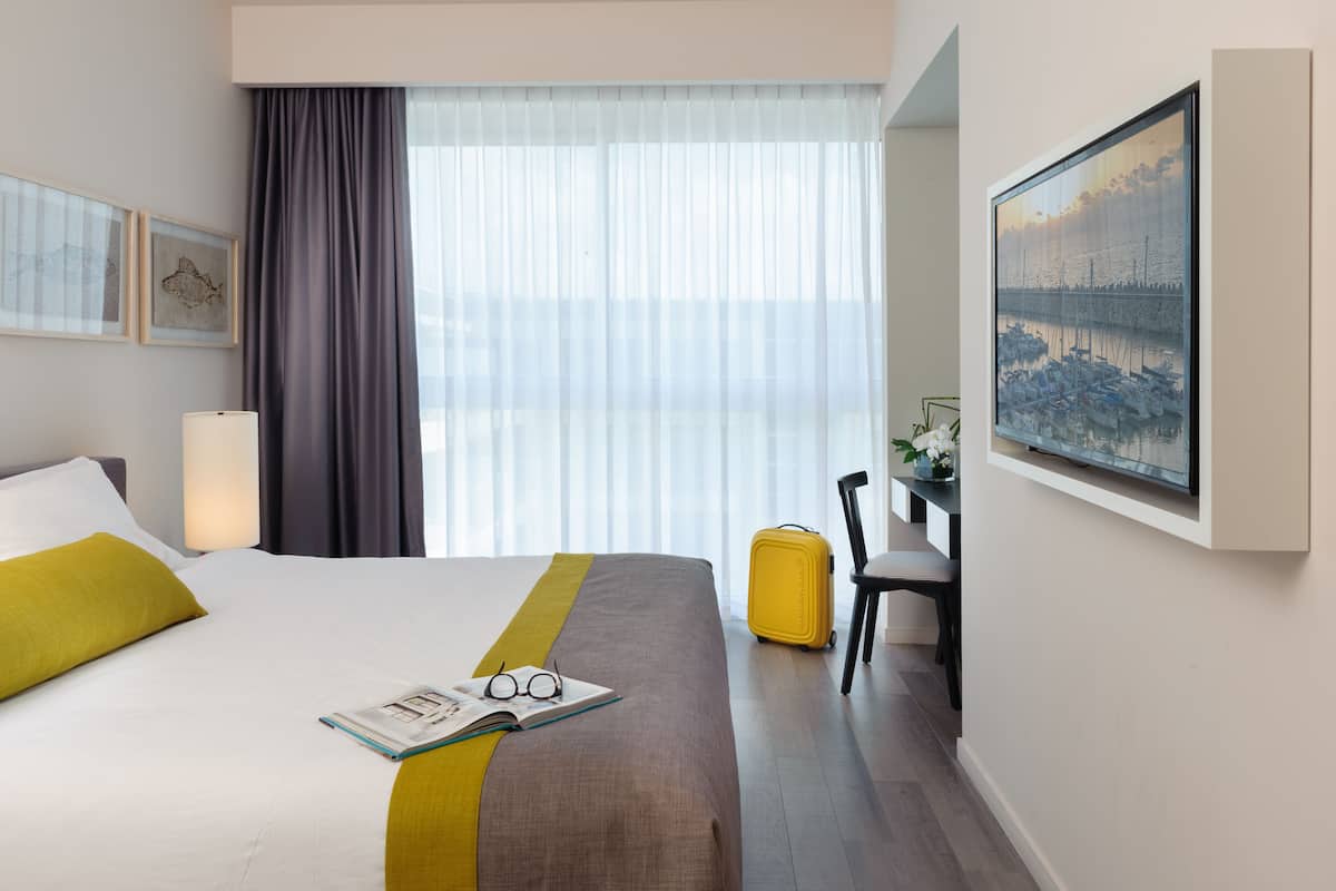 Een hotelkamer met een bed, een bureau, een stoel, een koffer en een schilderij aan de muur.