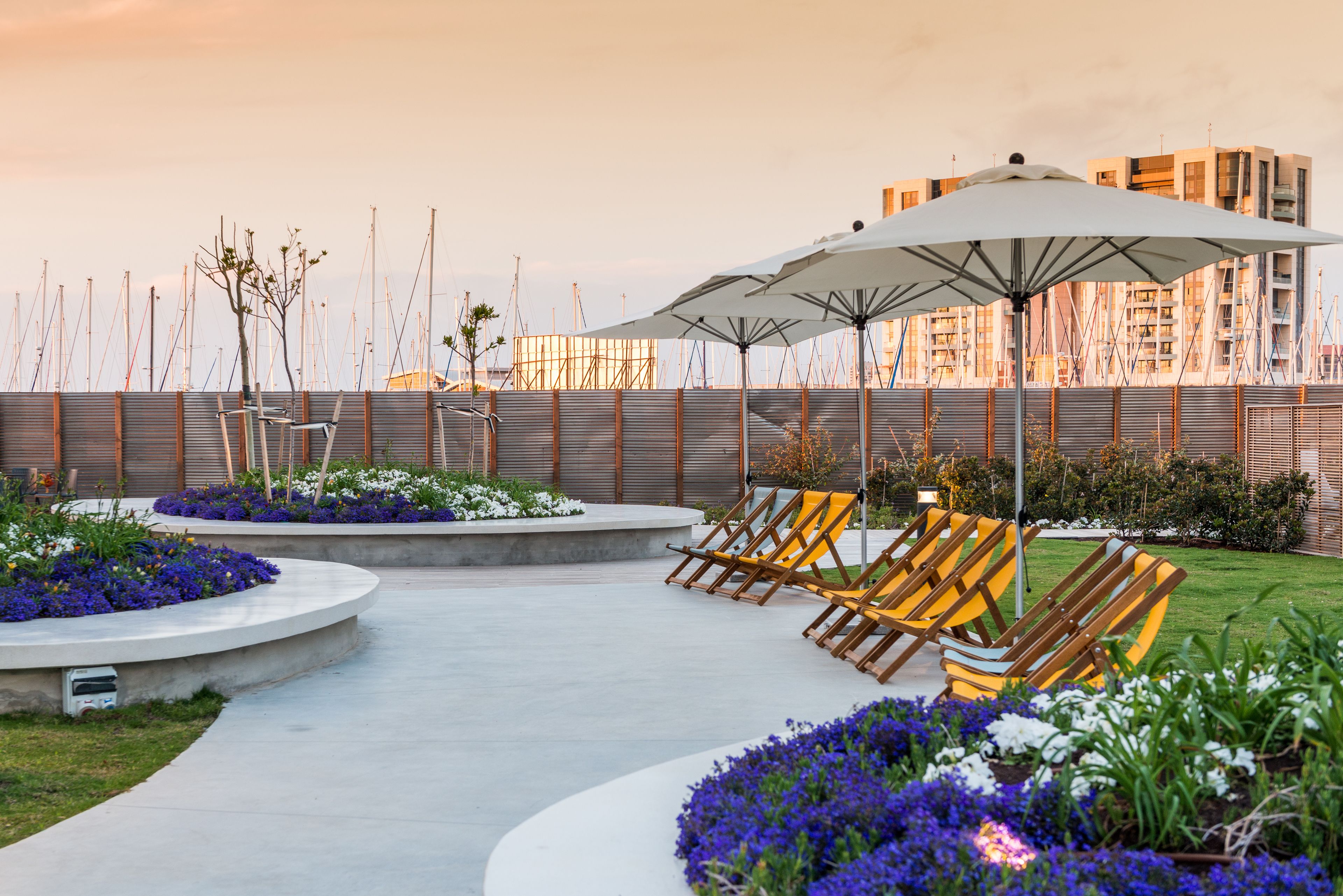 Un jardin sur le toit, avec des chaises longues, un grand parasol et une vue sur le paysage urbain.