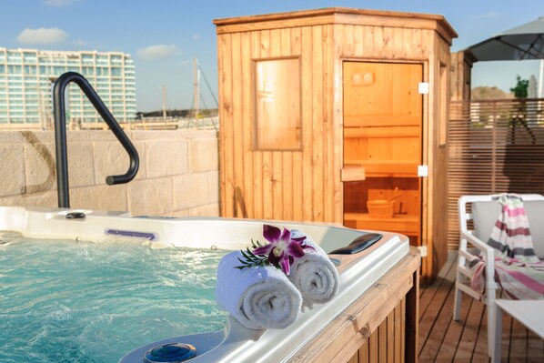 Una bañera de madera con dos toallas enrolladas y una orquídea púrpura decorativa, una cabaña de madera y una silla junto a la piscina.