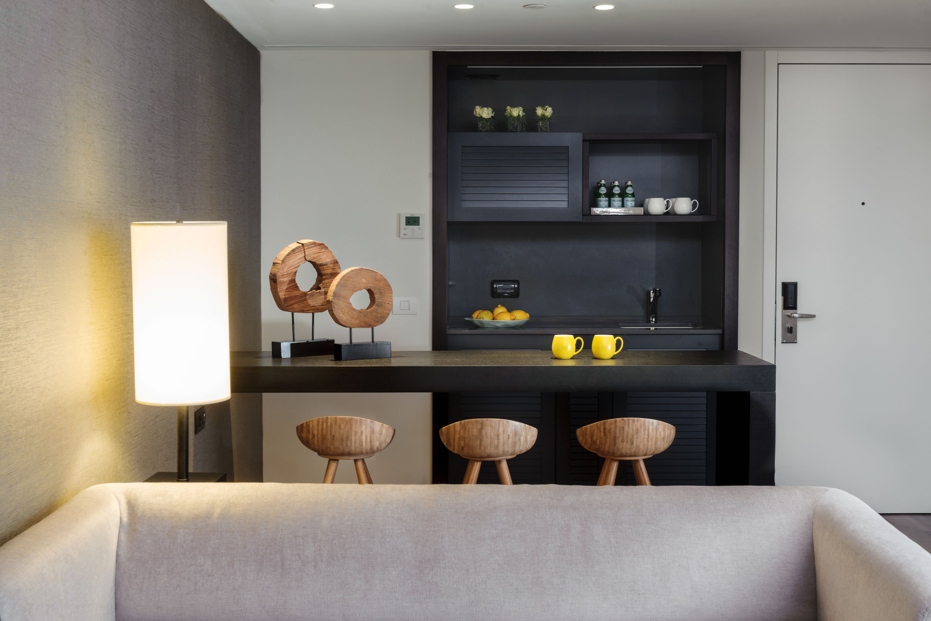 A modern room with a dark wood bar, a white lamp, and three wooden stools.