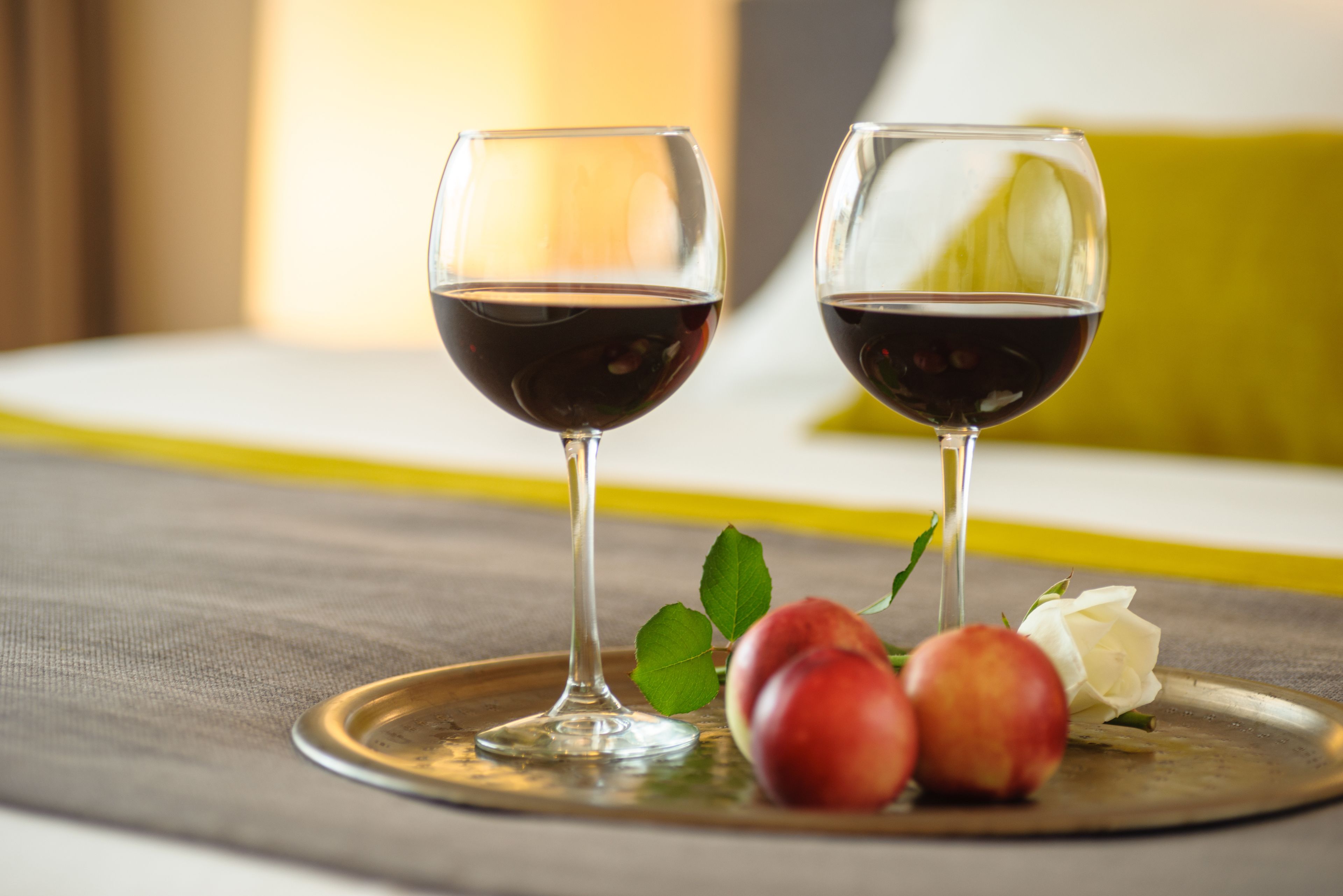 Two wine glasses on a tray with fruits and a flower.