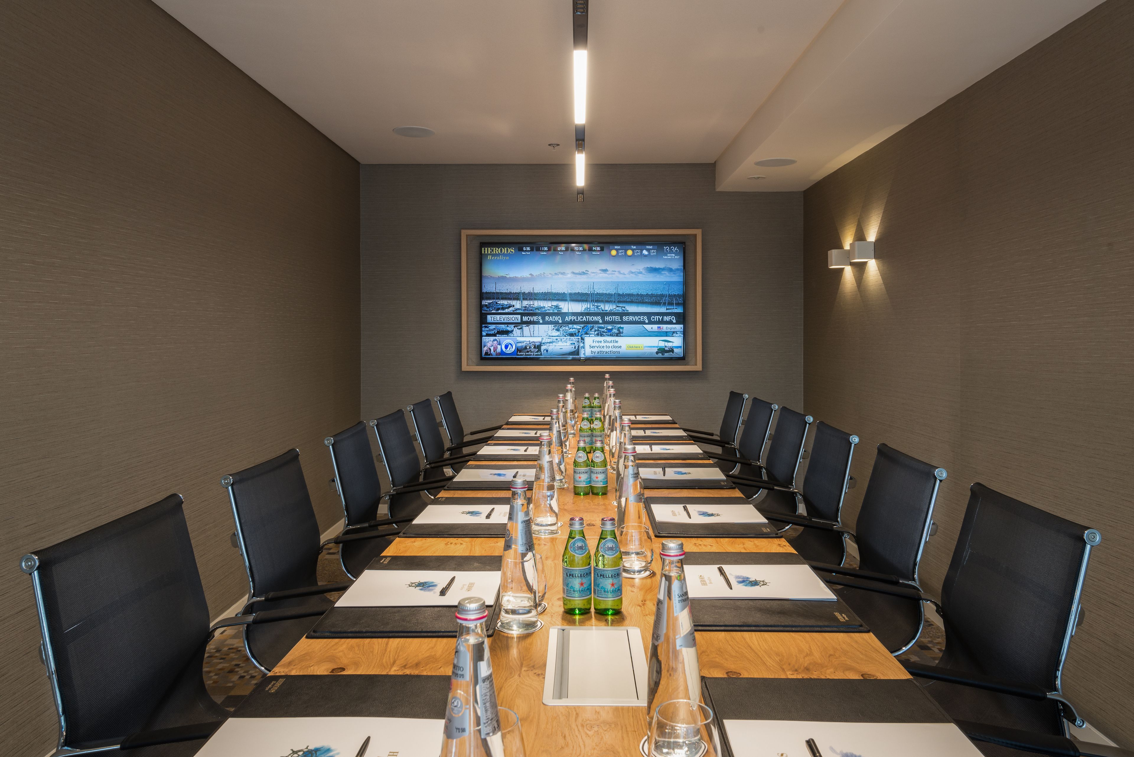 A conference room with a long table, chairs, and a screen displaying a news channel.