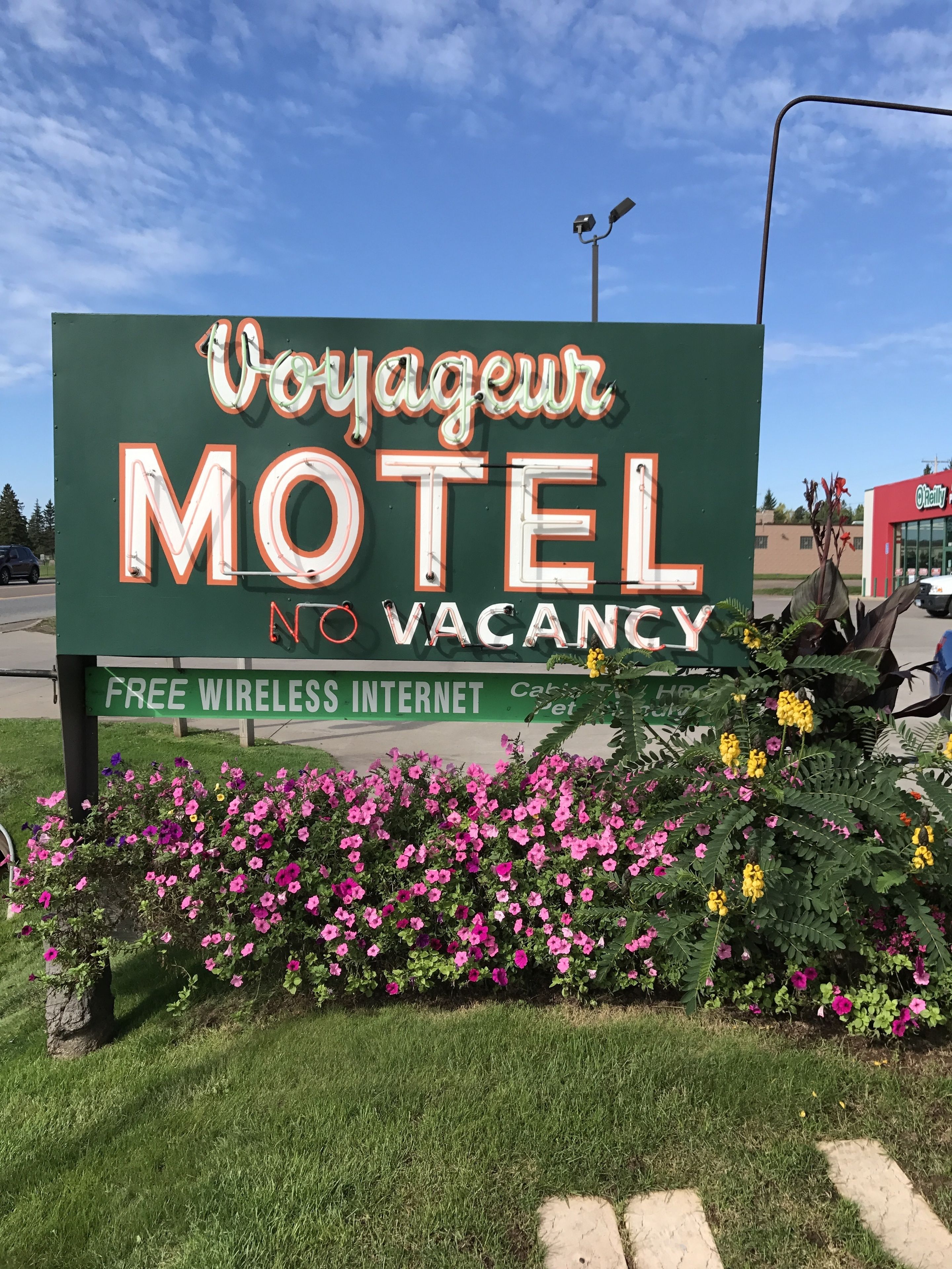 Et motel-skilt med teksten "Voyageur Motel" og "Udsolgt", omgivet af blomster og grøn vegetation.