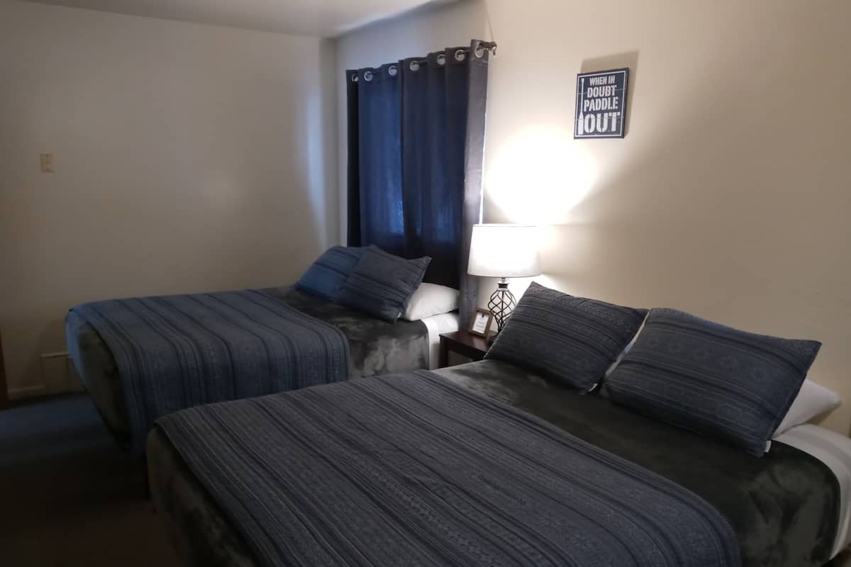 A room with two beds, a nightstand, a lamp, and a sign on the wall.