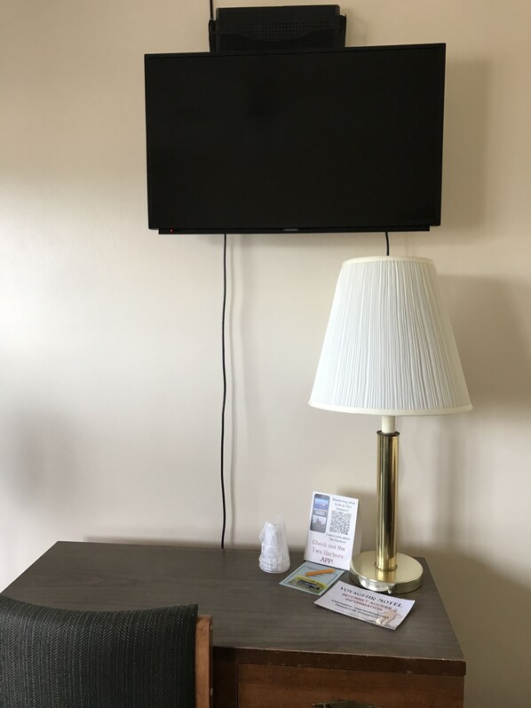 A hotel room with a flat-screen TV mounted on the wall, a table lamp, a small tissue box, and a QR code for the hotel app.