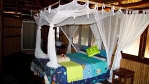 A bed with a canopy, a bedside table, and a window with curtains. - Casa Chibububo Lodge (Vilanculos)