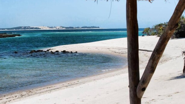 A beach with a thatched roof structure, clear turquoise water, and sandy shore. - Casa Chibububo Lodge (Vilanculos)