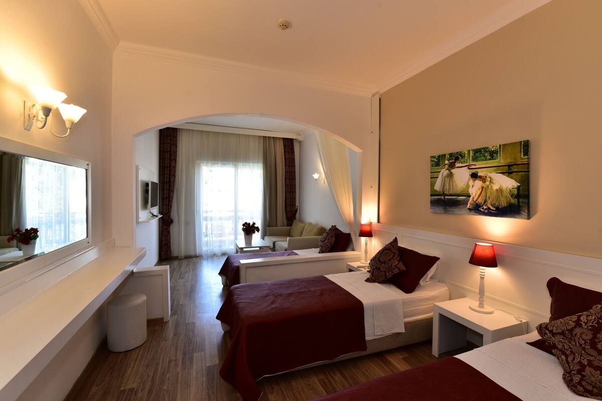 Une chambre d’hôtel avec deux lits, un coin salon, une grande fenêtre et un tableau au mur.