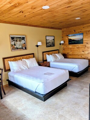 Quarto com duas camas, teto de madeira, luminárias fixadas na parede e quadros emoldurados.