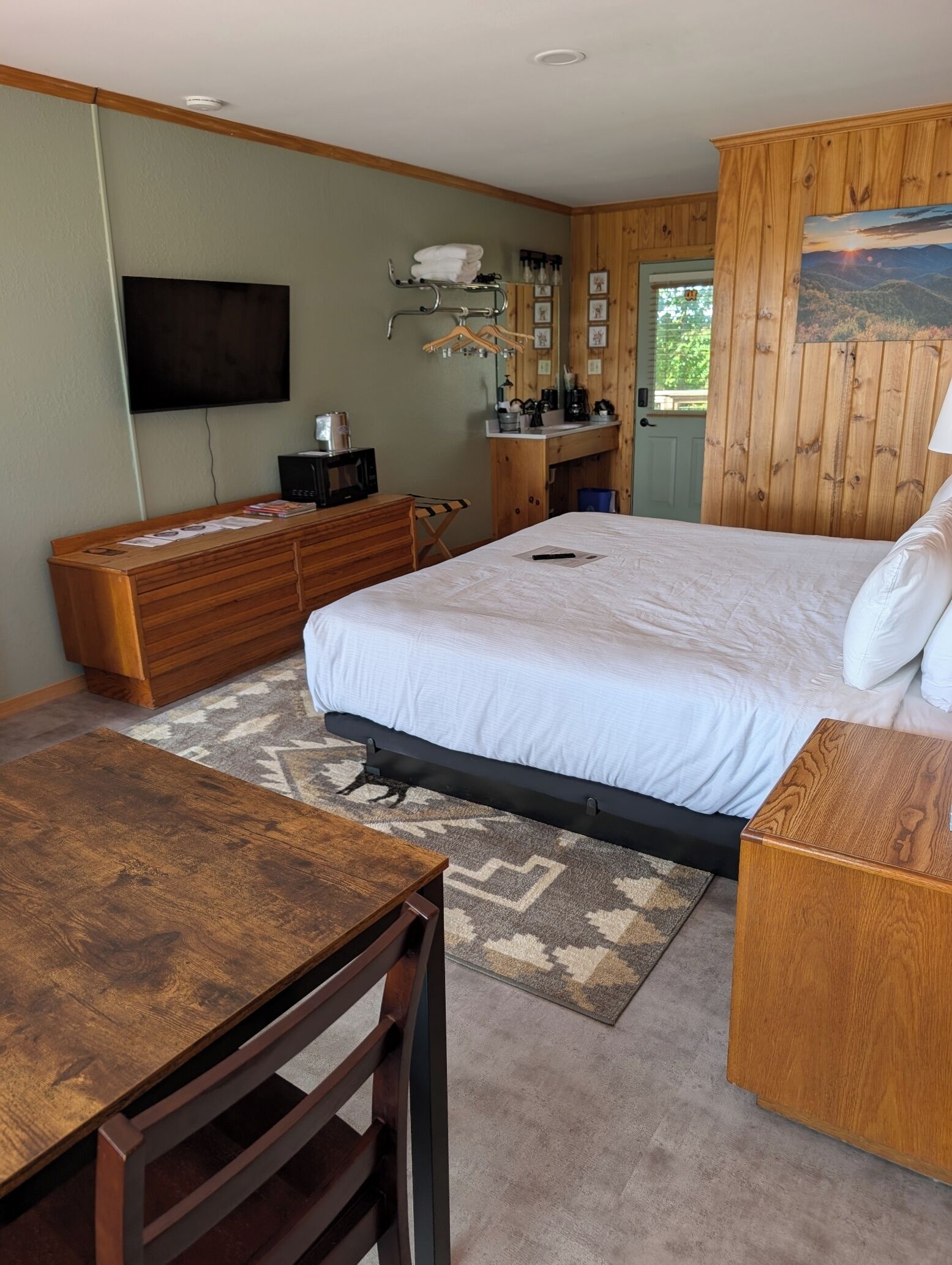 A bedroom with a bed, wooden dresser, desk, and a television on the wall.