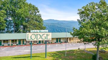 A lodge with a green roof, a parking lot, and a sign that reads "Saluda Mountain LODGE".