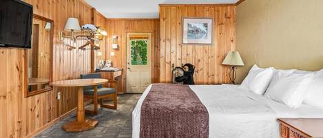 A wooden-paneled room with a bed, a desk, a chair, a television, and a door.
