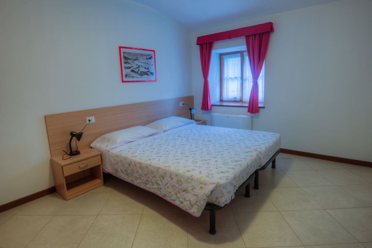 Een slaapkamer met een bed, nachtkastje, lamp en een raam met gordijnen.