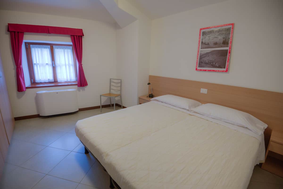 Een slaapkamer met een groot bed, een raam met gordijnen, een stoel en een lijst met een afbeelding aan de muur.
