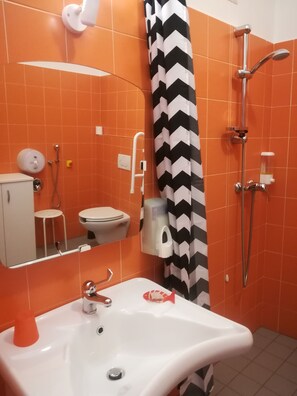 Un bany amb rajoles taronges, un lavabo blanc, un vàter, un mirall, una dutxa i una cortina de dutxa amb dibuixos de franges negres i blanques.